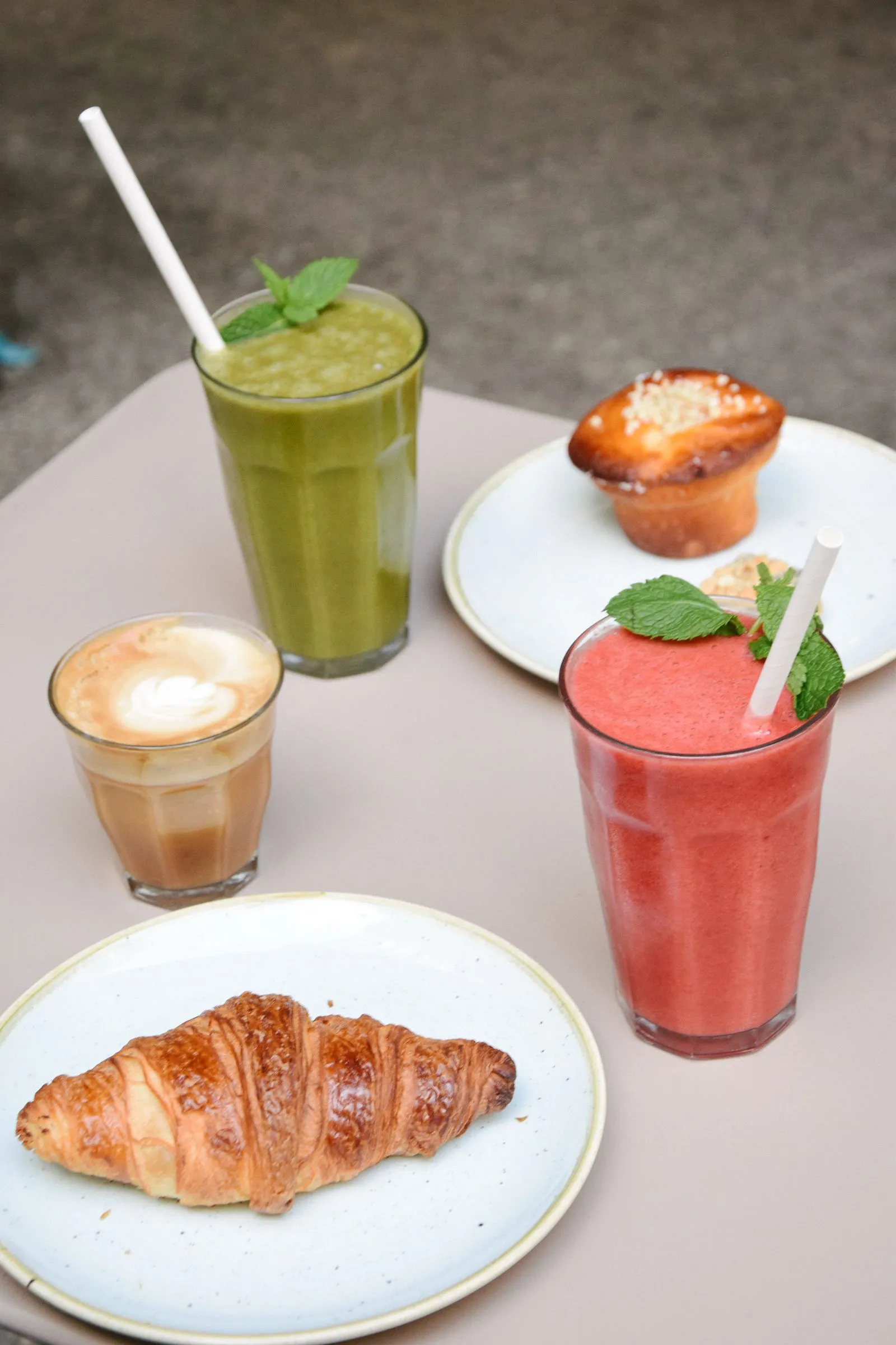 +Teller mit einem Croissant und einem Muffin. Außerdem zwei frische Smoothies und ein Kaffee.