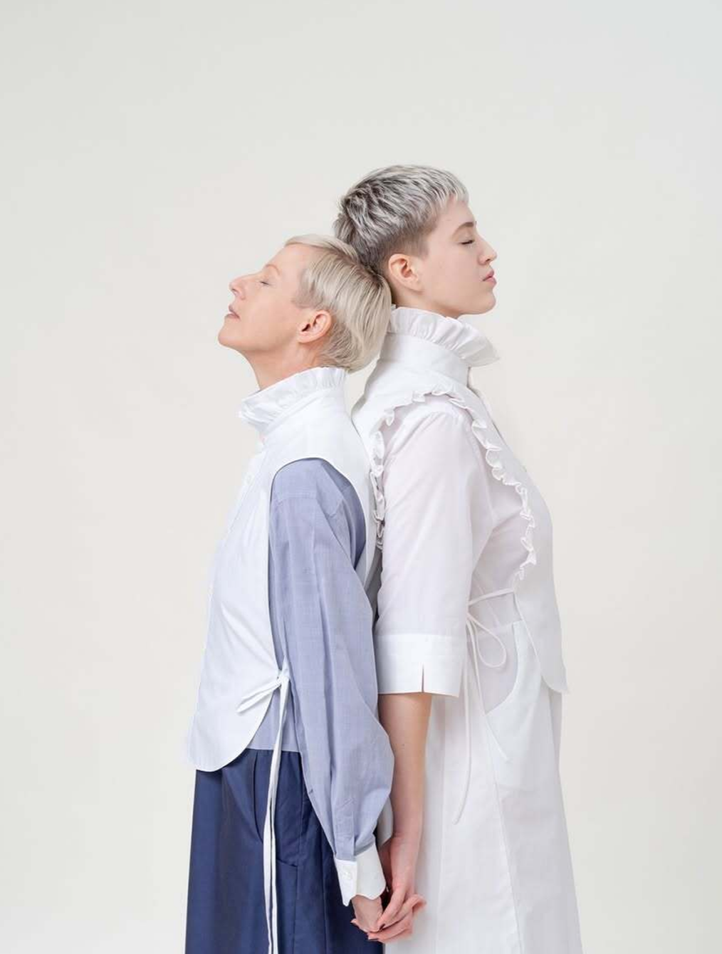 Zwei Frauen mit kurzen Haaren, rücken an rücken im Ganzkörper-Profil 