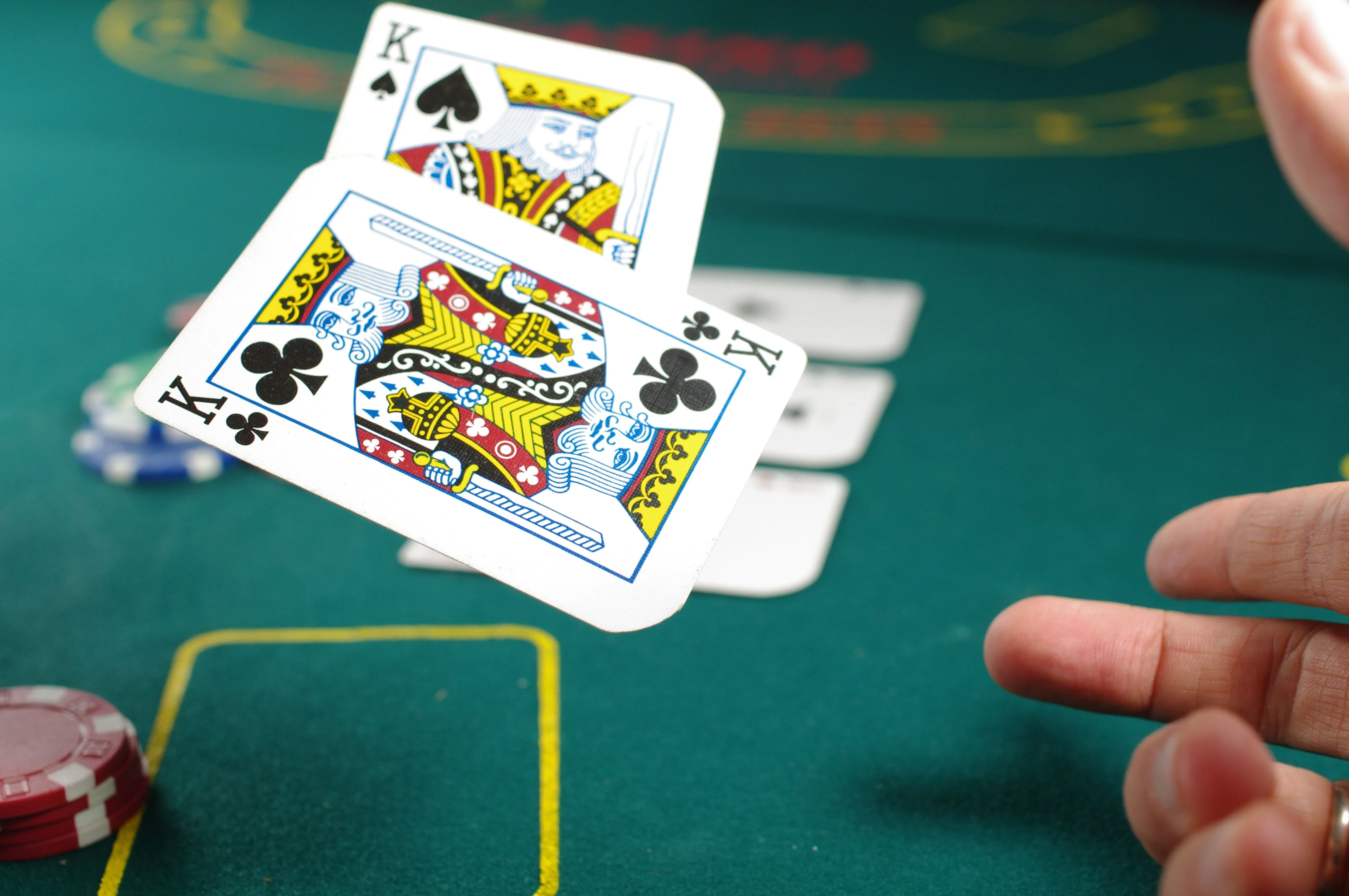 Nahaufnahme eines Pokertisches mit zwei aufgedeckten Königen (Karo und Kreuz) in einer Hand. Im Hintergrund sind weitere Spielkarten und Pokerchips zu sehen.
